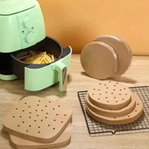 Gelochte helle Einlagen gestapelt neben einem Airfryer, daneben Pommes